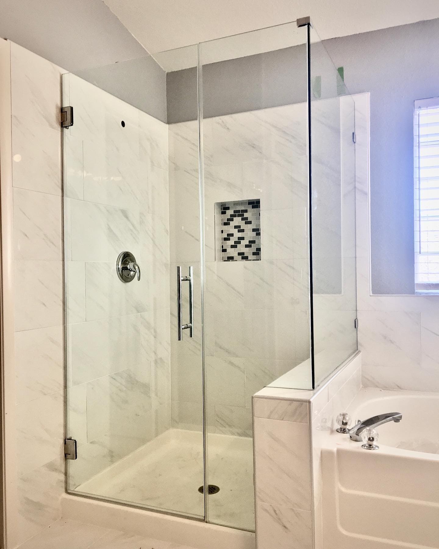 L-shaped shower enclosure with marble tile and chrome hardware