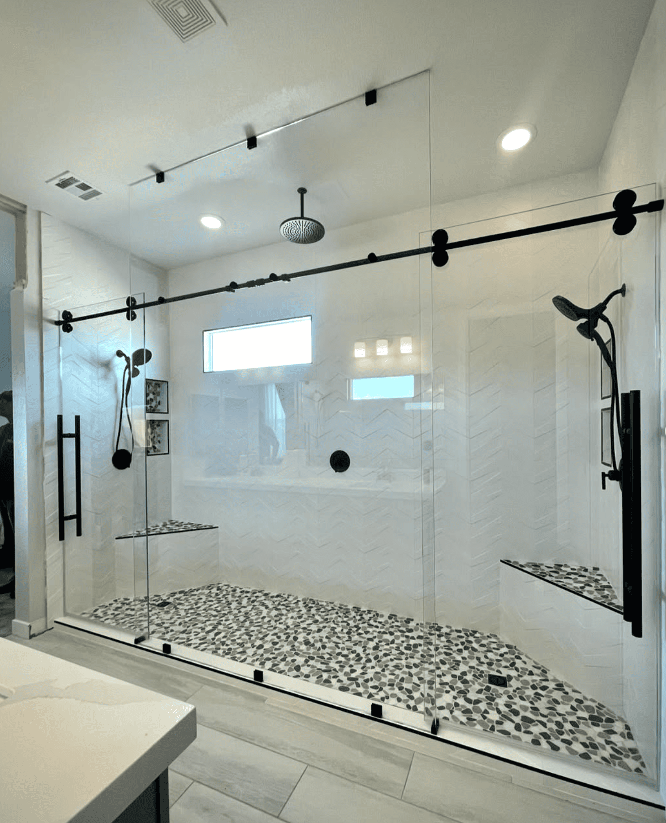 Modern frameless sliding shower doors with black hardware and pebble tile flooring by Baja Glass Las Vegas